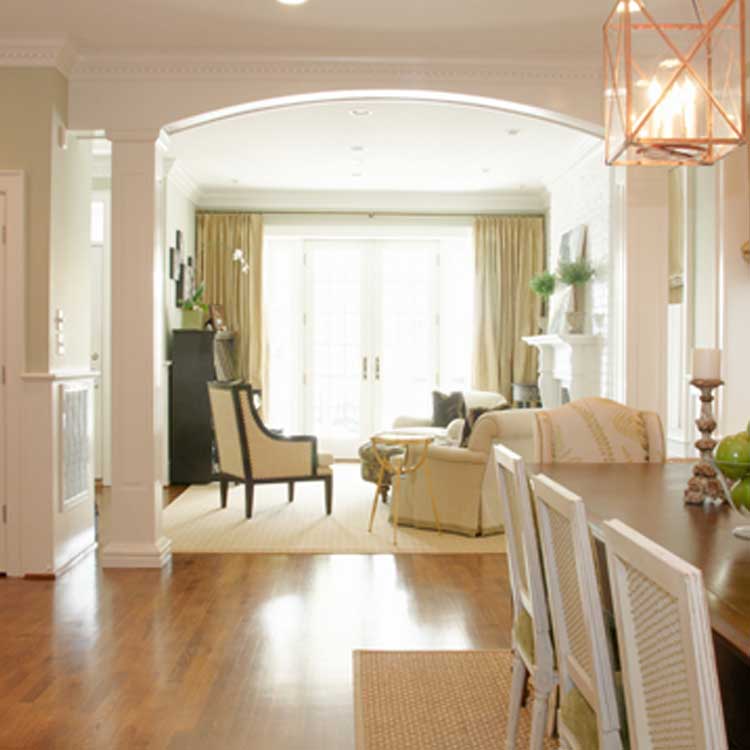 A view through columns from a dining room into a living room with hardwood floors and a large window