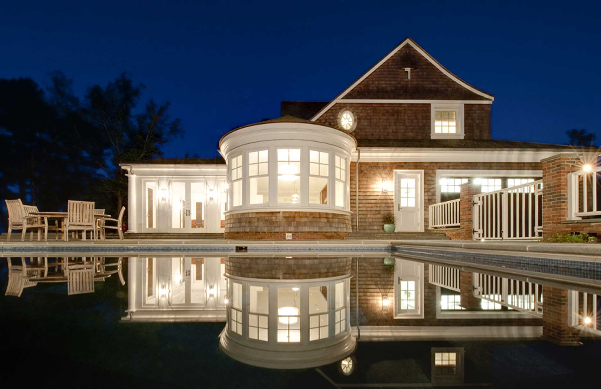 A backyard at night with lights reflecting on the pool in Little Neck built by Covington Contracting luxury custom homebuilder in Hampton Roads Virginia